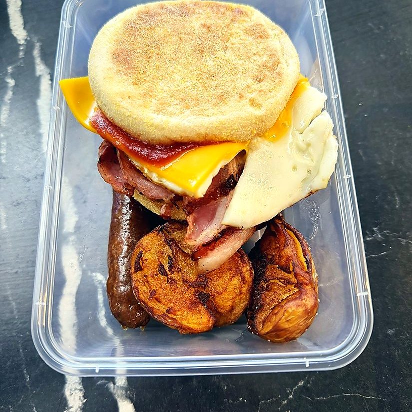 Breakfast crib of a bacon, egg and cheese muffin with sausage and hash brown, packed to go