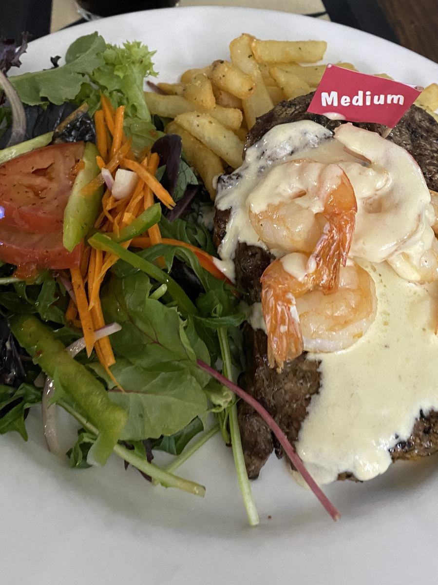 Steak topped with garlic prawns and creamy sauce, with salad and chips